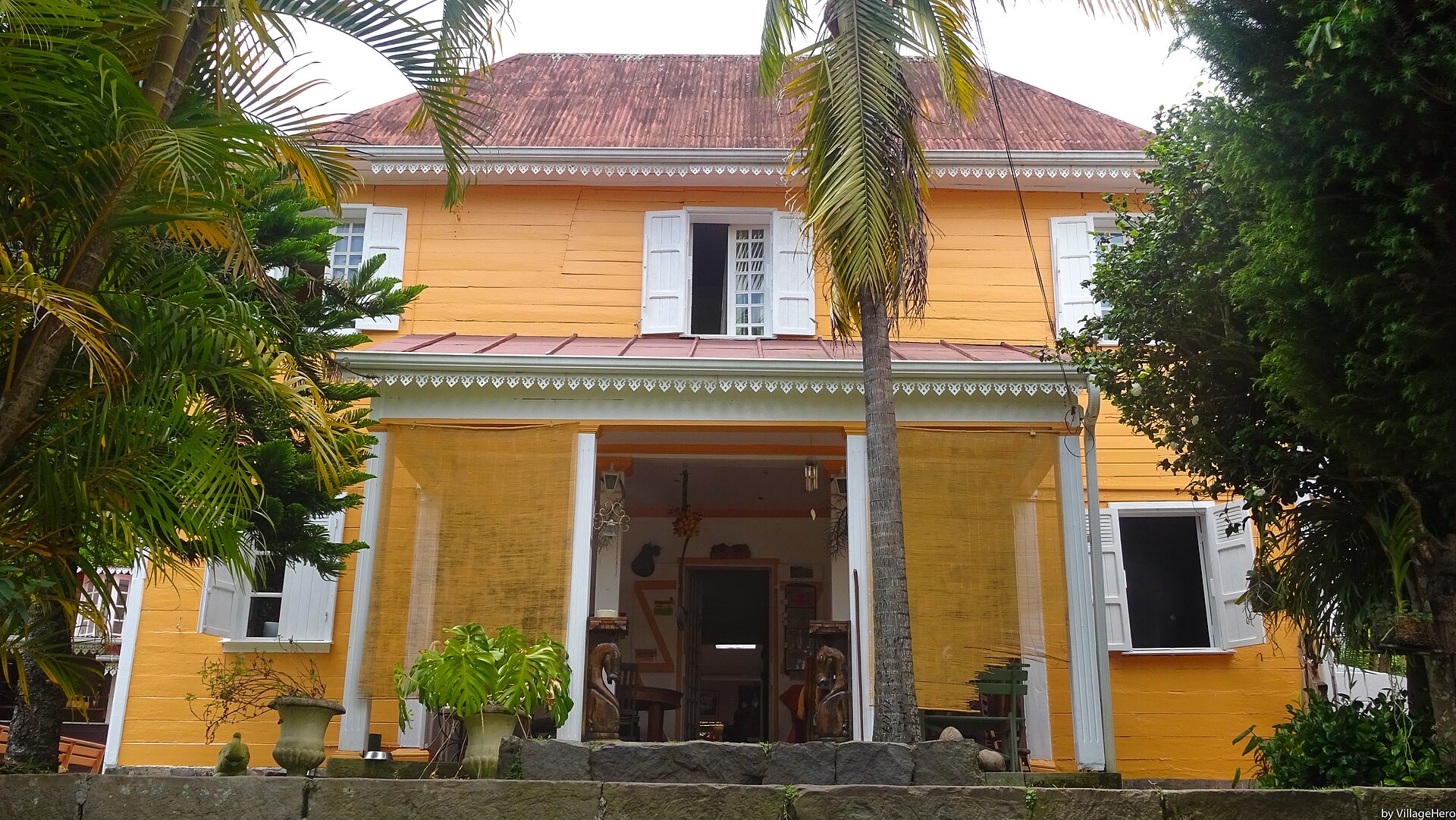 Une villa créole jaune à Hell-Bourg, avec sa varangue, ses lambrequins et son jardin planté