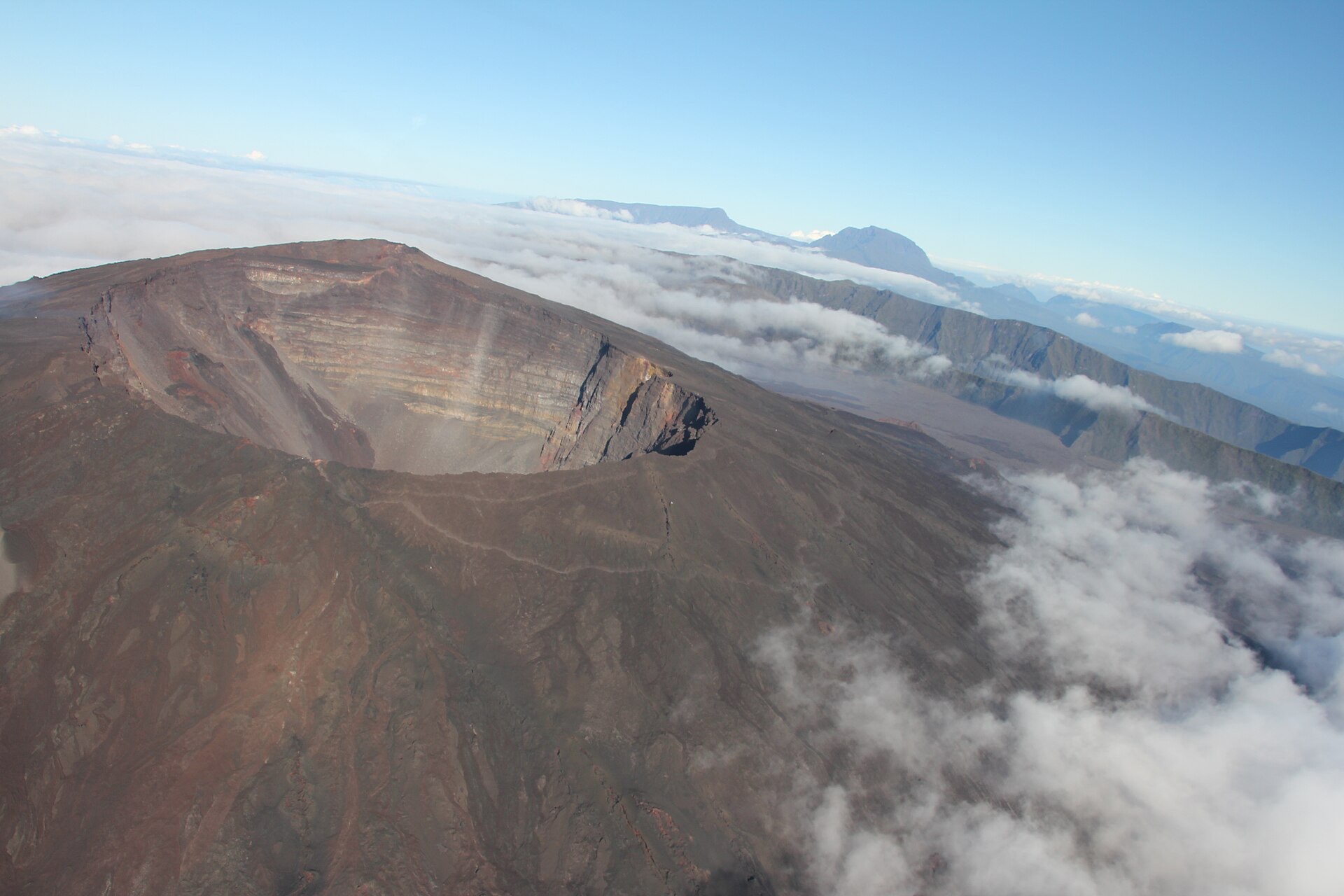 Le cratère Dolomieu du Piton de la Fournaise vu d'en haut, le cône sombre posé sur l'enclos et la mer de nuages